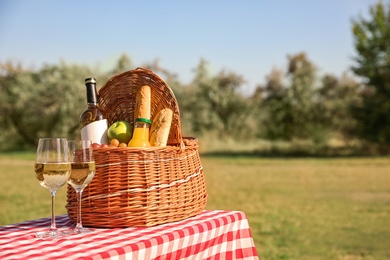 Photo of Wicker picnic basket with wine and snacks on table in park. Space for text