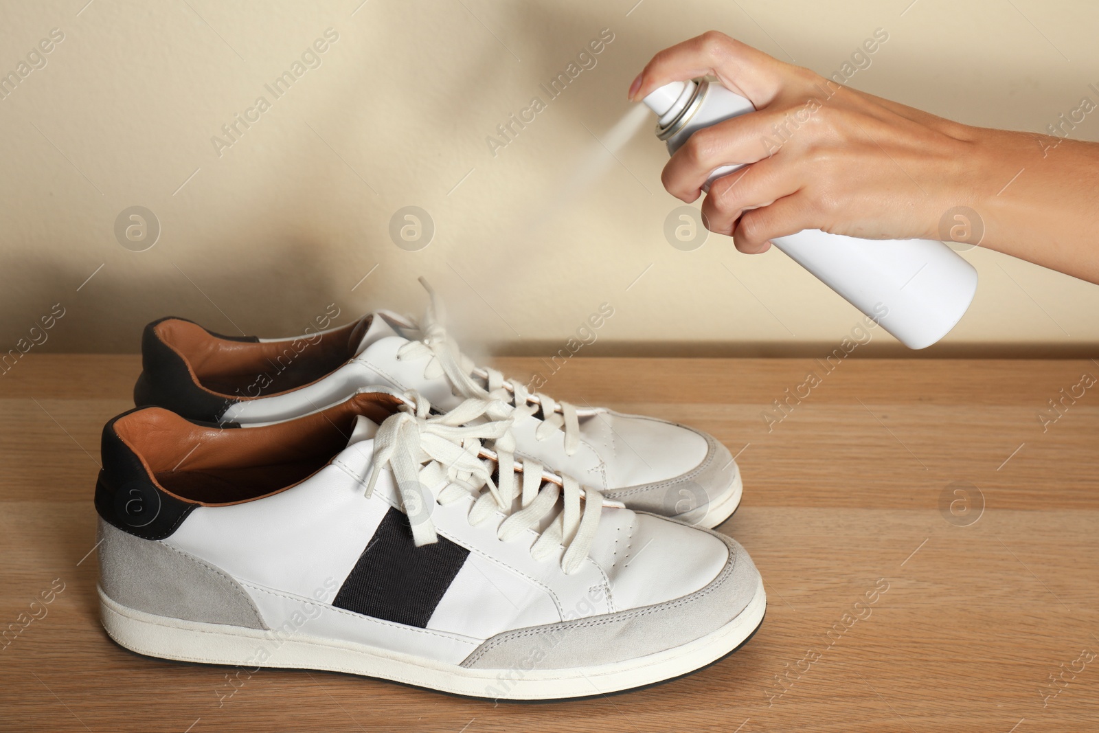 Image of Woman spraying deodorant over pair of shoes at home, closeup