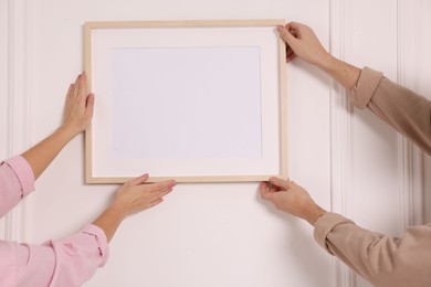 Man and woman hanging picture frame on white wall, closeup