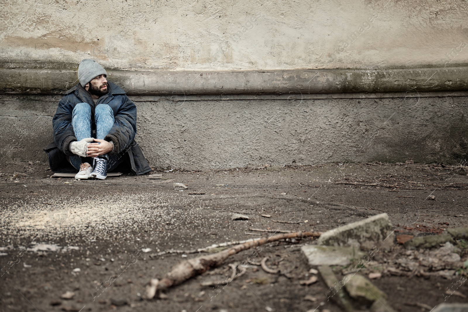 Photo of Poor homeless man sitting near wall on street. Space for text