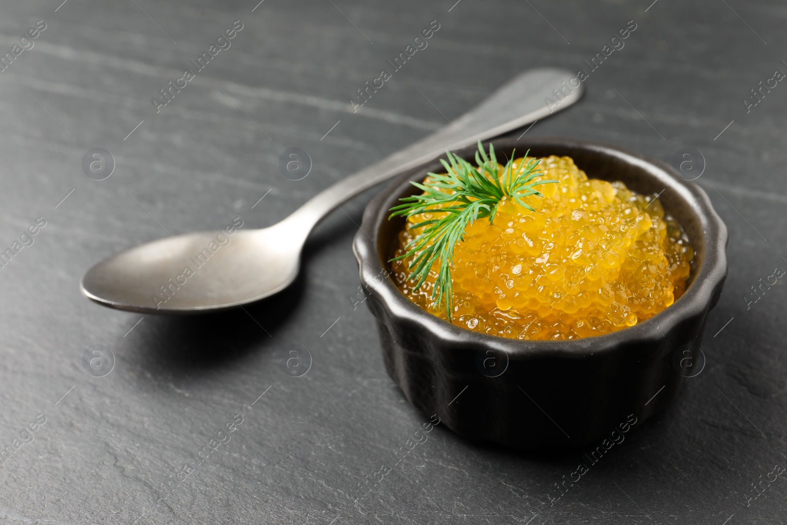 Photo of Fresh pike caviar in bowl and spoon on black table