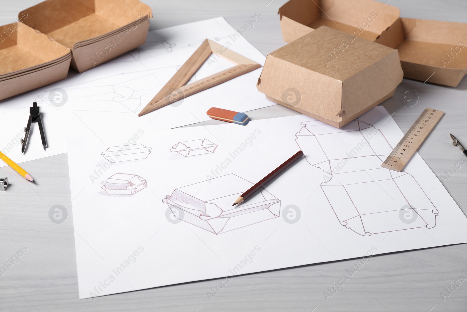 Photo of Creating packaging design. Drawings, boxes and stationery on light wooden table, closeup