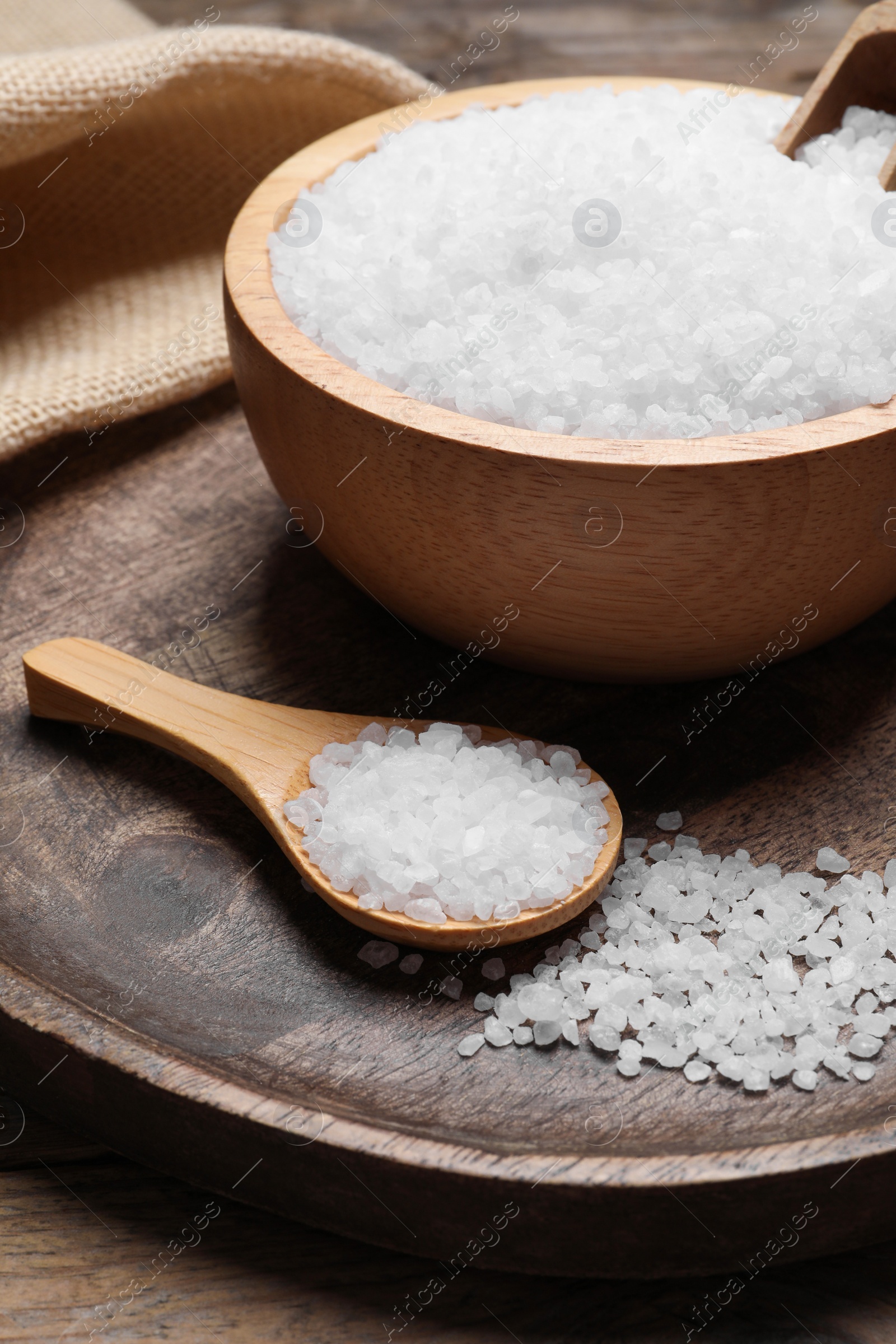 Photo of Bowl and spoon with natural sea salt on wooden table, closeup