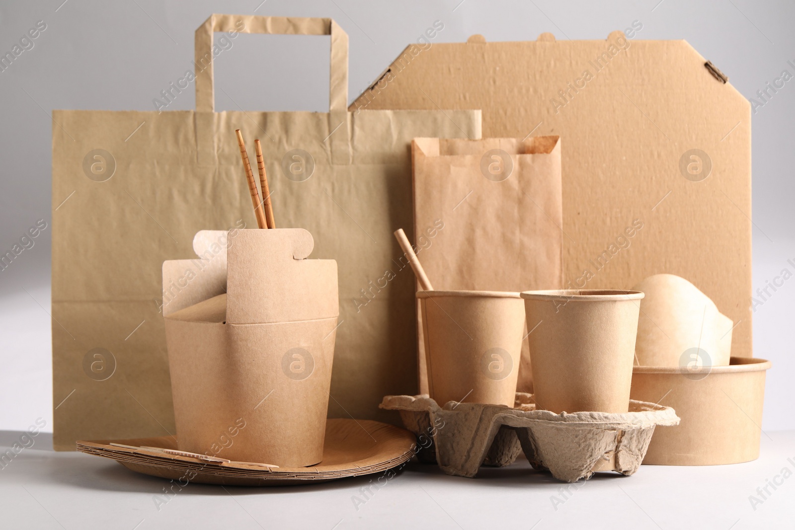 Photo of Eco friendly food packaging. Paper containers, tableware and bag on light background