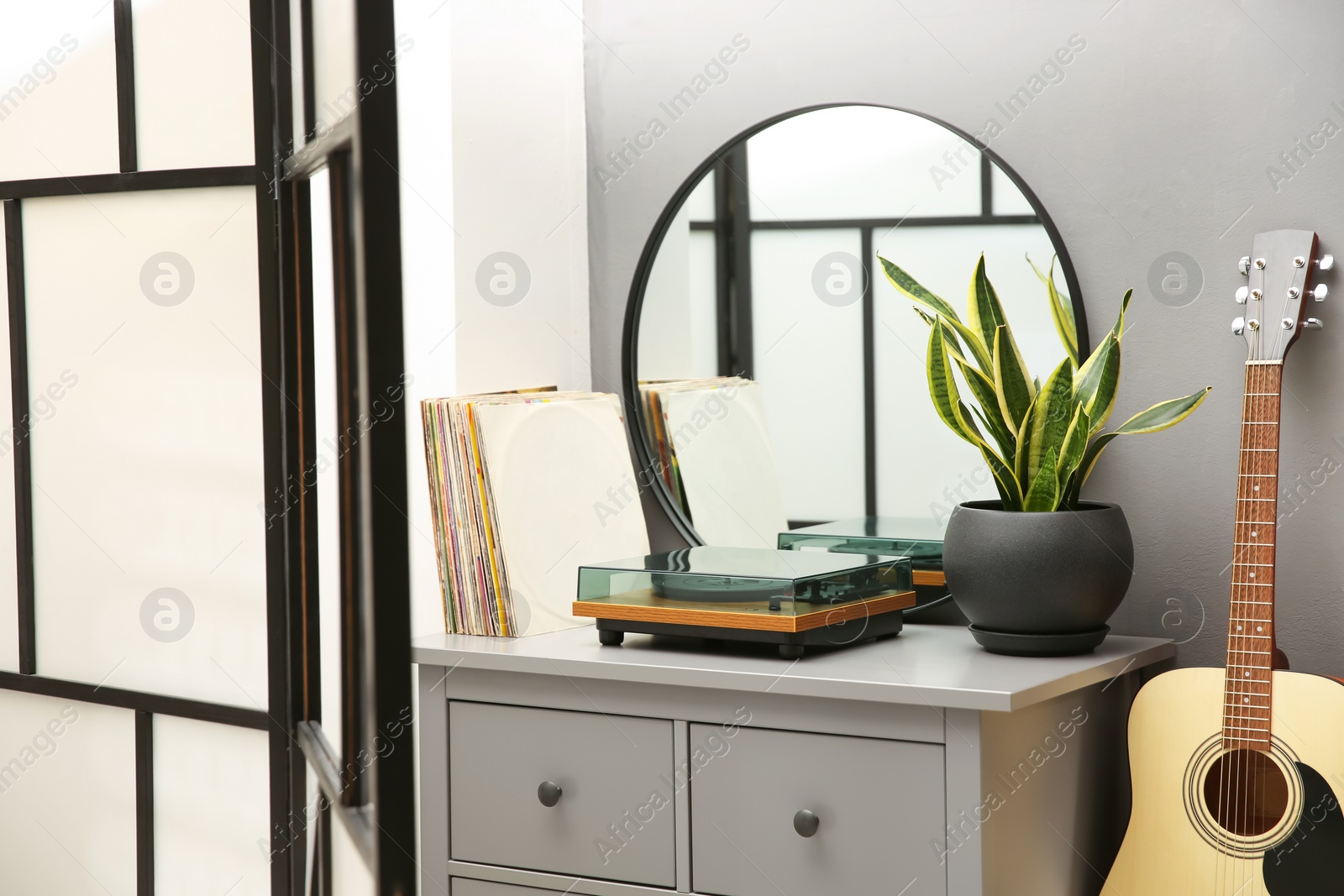 Photo of Stylish turntable, guitar and vinyl records on chest of drawers indoors