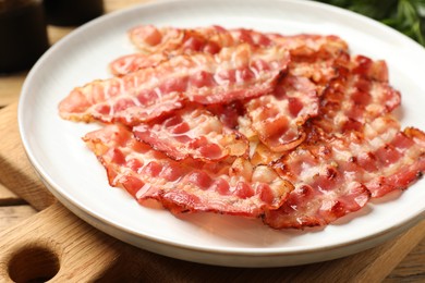 Photo of Plate with fried bacon slices on wooden table, closeup