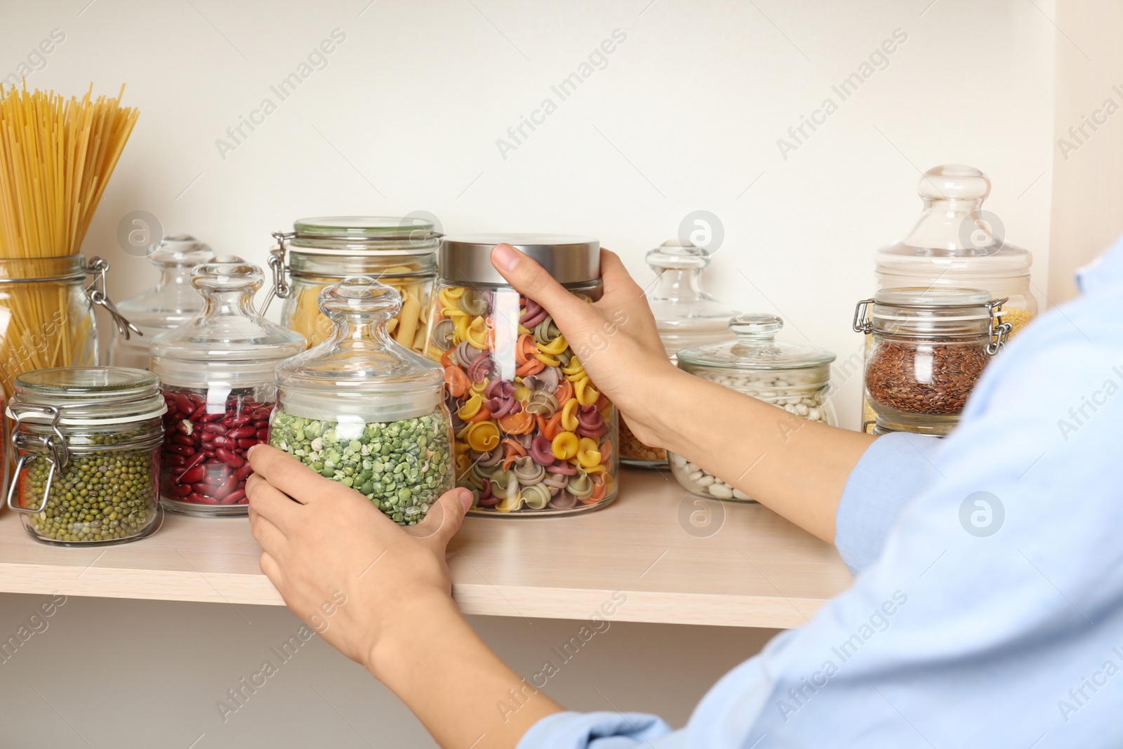 Photo of Woman taking jars of different products from wooden shelf, closeup