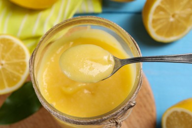 Taking delicious lemon curd from jar at light blue table, closeup