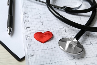 Photo of Cardiogram report, red decorative heart and stethoscope on table, closeup