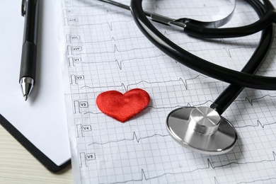 Cardiogram report, red decorative heart and stethoscope on table, closeup