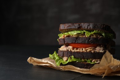 Photo of Delicious sandwich with tuna, tomatoes and lettuce on black table, space for text