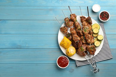 Metal skewers with delicious meat and vegetables served on light blue wooden table, flat lay. Space for text