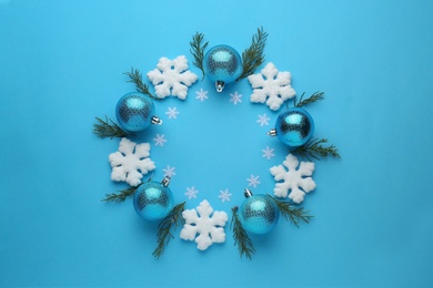 Photo of Bright festive wreath made of Christmas balls, decorative snowflakes and fir branches on light blue background, top view. Space for text
