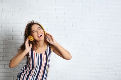 Photo of African-American woman listening to music with headphones near brick wall, space for text