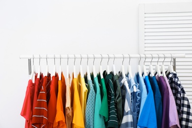 Photo of Rack with bright clothes in room. Rainbow colors