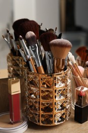 Set of professional brushes and makeup products near mirror on wooden table