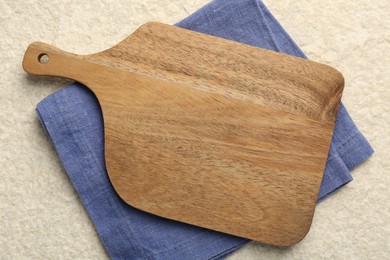 Photo of Wooden cutting board and napkin on beige table, top view. Space for text