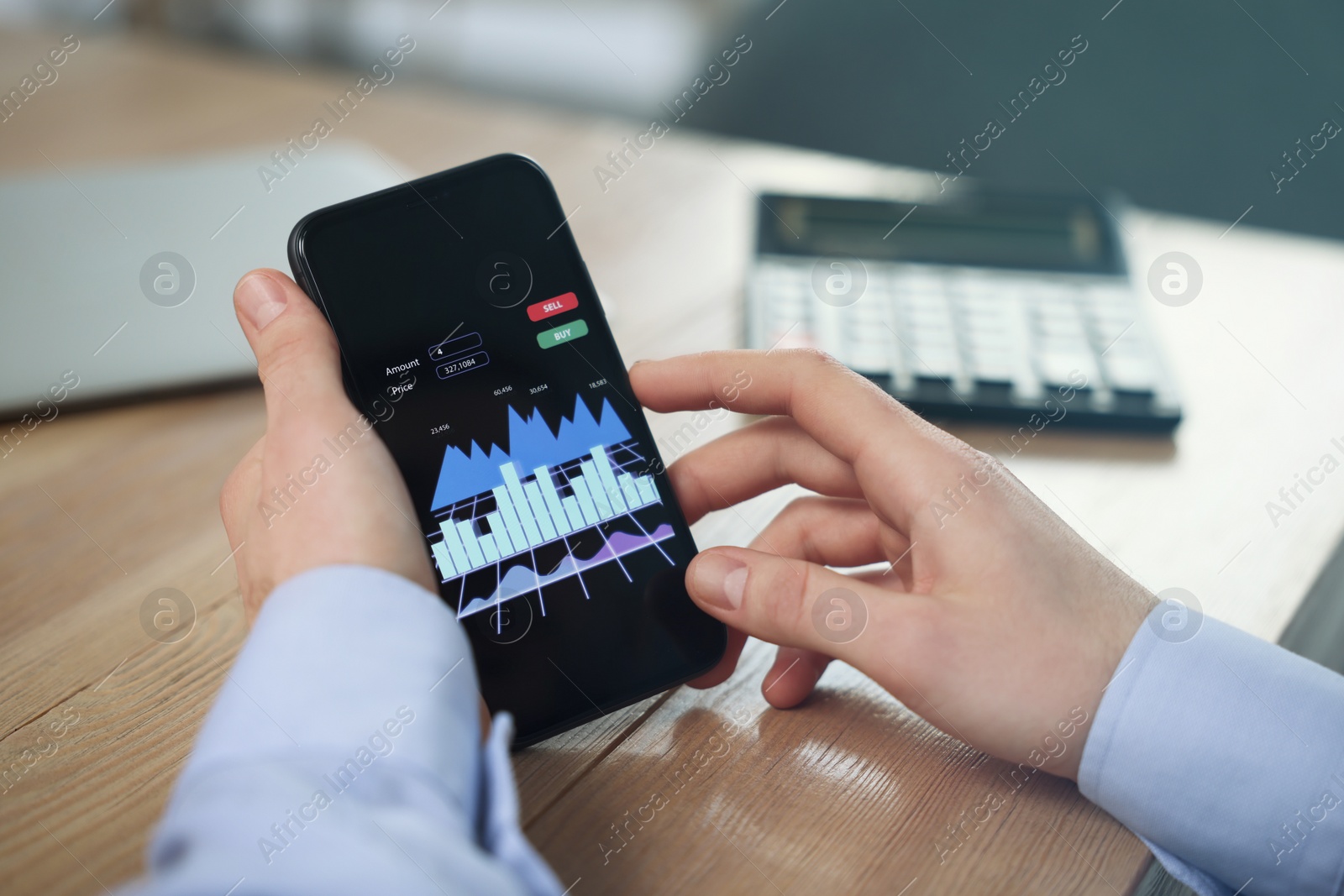 Photo of Forex trader with smartphone working at wooden table, closeup