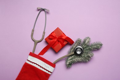 Photo of Greeting card for doctor with stethoscope, gift box and Christmas decor on purple background, flat lay