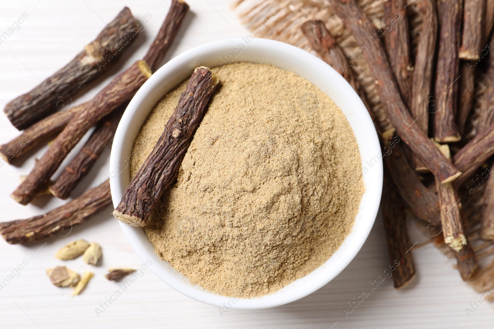 Photo of Powder in bowl and dried sticks of liquorice root on white table, flat lay