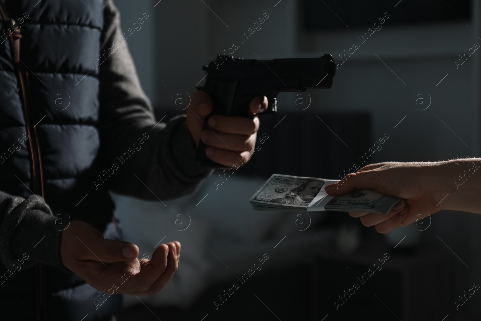 Photo of Woman giving money to criminal with gun indoors, closeup. Armed robbery