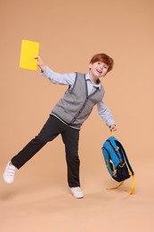 Photo of Happy schoolboy with book and backpack on beige background