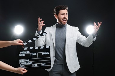 Photo of Emotional actor performing while second assistant camera holding clapperboard on black background