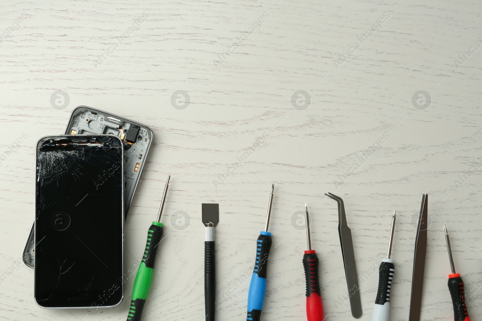 Photo of Damaged smartphone and repair tools on white wooden background, flat lay. Space for text