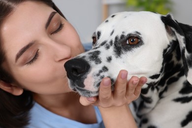 Photo of Beautiful woman kissing her adorable Dalmatian dog indoors, closeup. Lovely pet