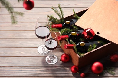 Photo of Wooden crate with bottles of wine, glasses, fir twigs and red Christmas balls on table. Space for text