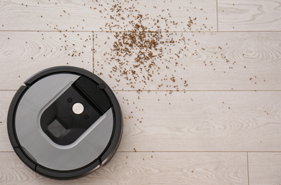 Modern robotic vacuum cleaner removing scattered buckwheat from wooden floor, top view. Space for text