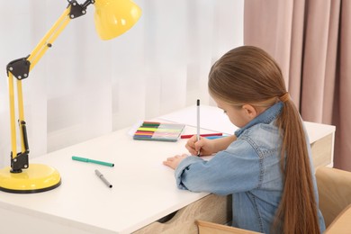 Photo of Cute little girl drawing with markers at desk in room. Home workplace