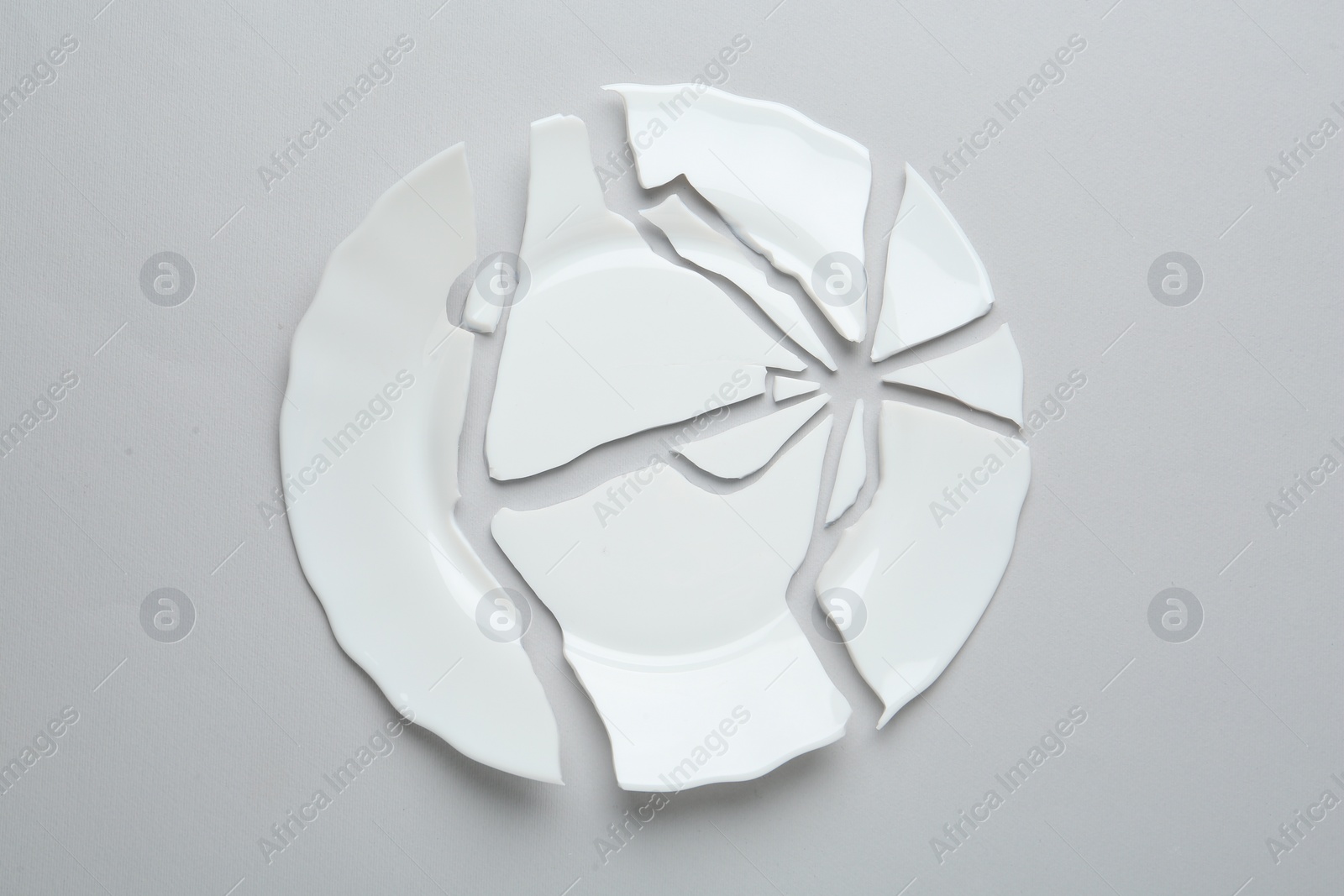 Photo of Pieces of broken ceramic plate on light grey background, flat lay