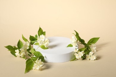 Photo of Presentation of product. White podium and beautiful jasmine flowers on beige background, space for text