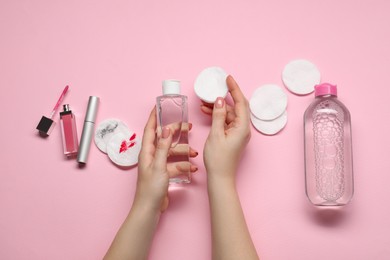 Photo of Woman with makeup remover, cotton pads, cosmetic product, lip gloss and mascara on pink background, top view