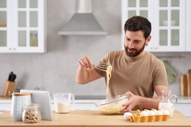 Man making dough while watching online cooking course via tablet in kitchen