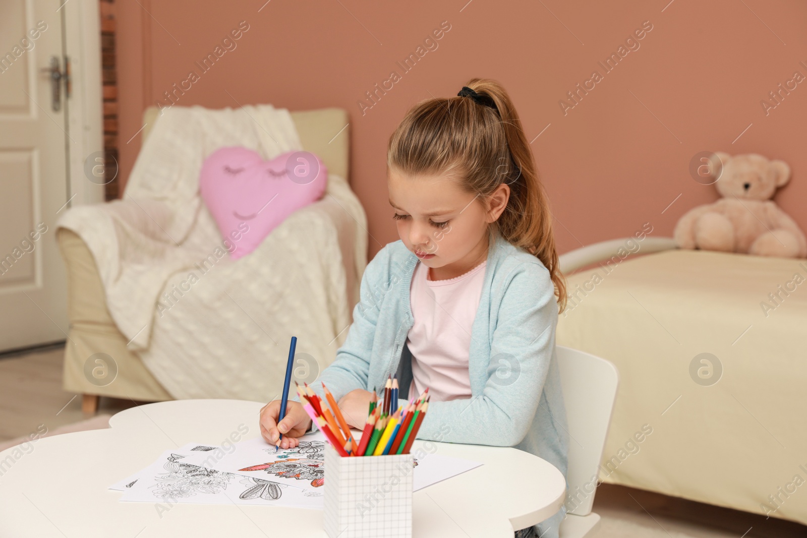 Photo of Little girl coloring antistress page at table indoors