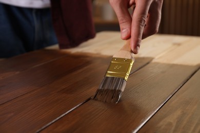 Photo of Man with brush applying wood stain onto wooden surface, closeup
