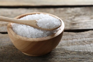 Photo of Organic salt in bowl and spoon on wooden table, closeup. Space for text