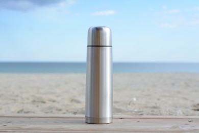 Photo of Metallic thermos with hot drink on wooden surface near sea
