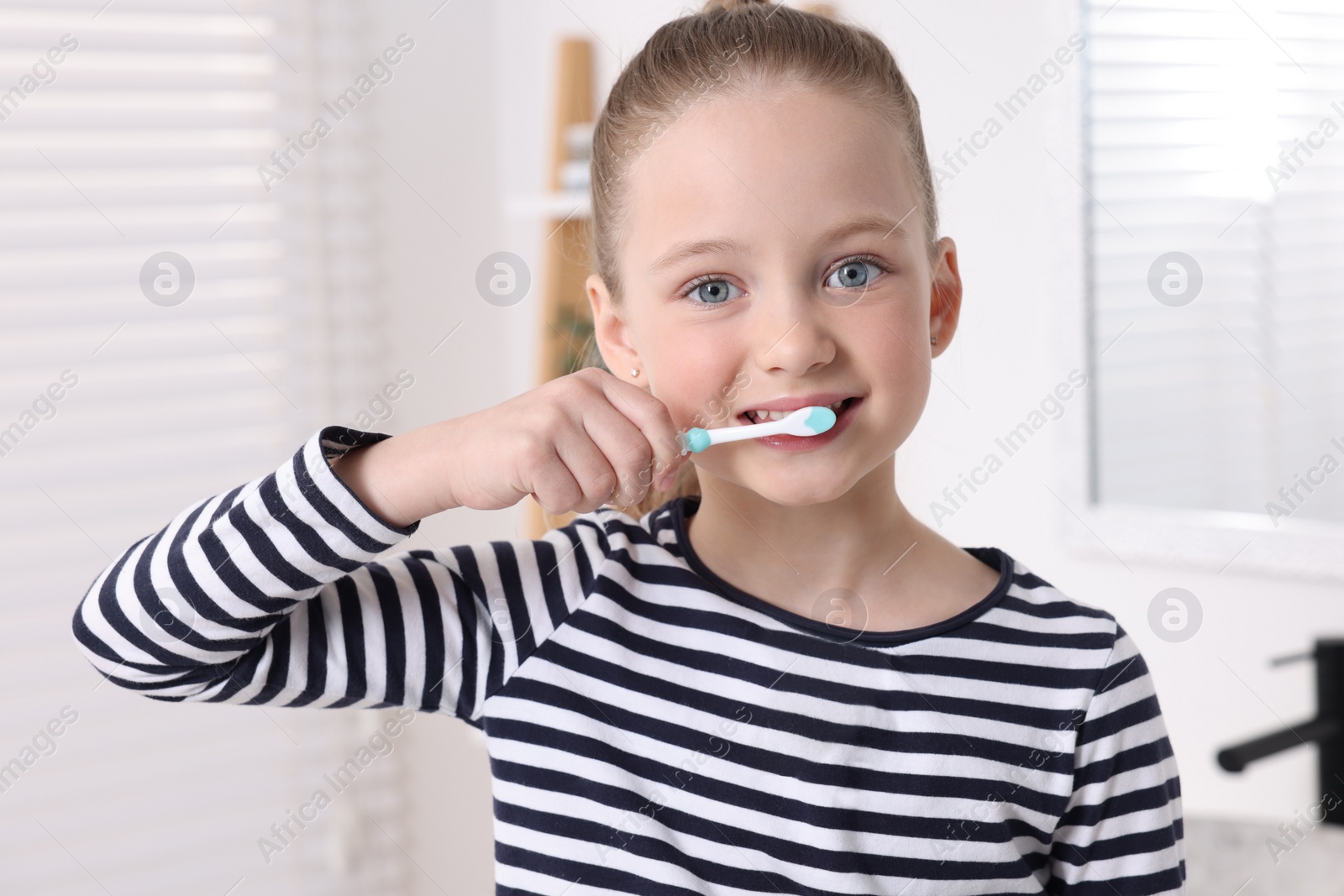 Photo of Cute little girl brushing her teeth with plastic toothbrush in bathroom