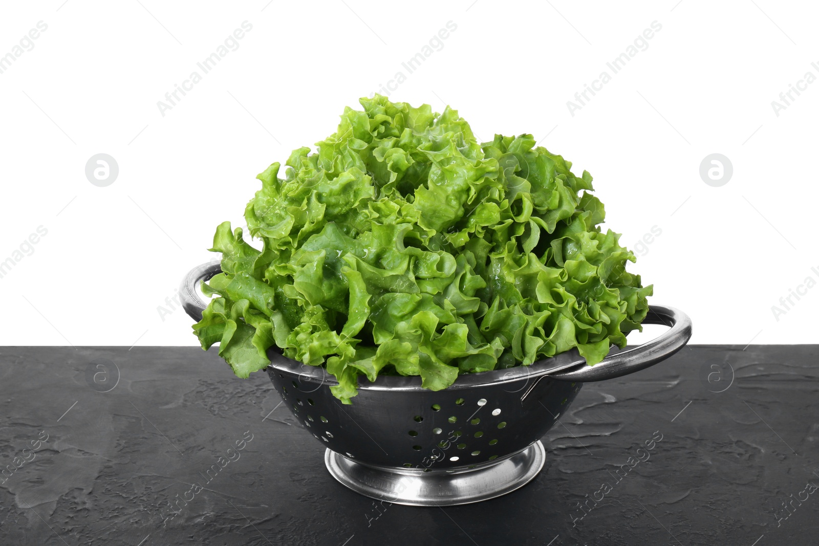 Photo of Metal colander with fresh lettuce on black textured table against white background