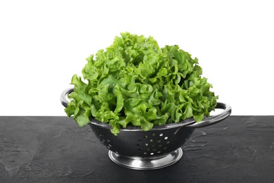 Photo of Metal colander with fresh lettuce on black textured table against white background