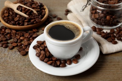 Cup of aromatic hot coffee and beans on wooden table