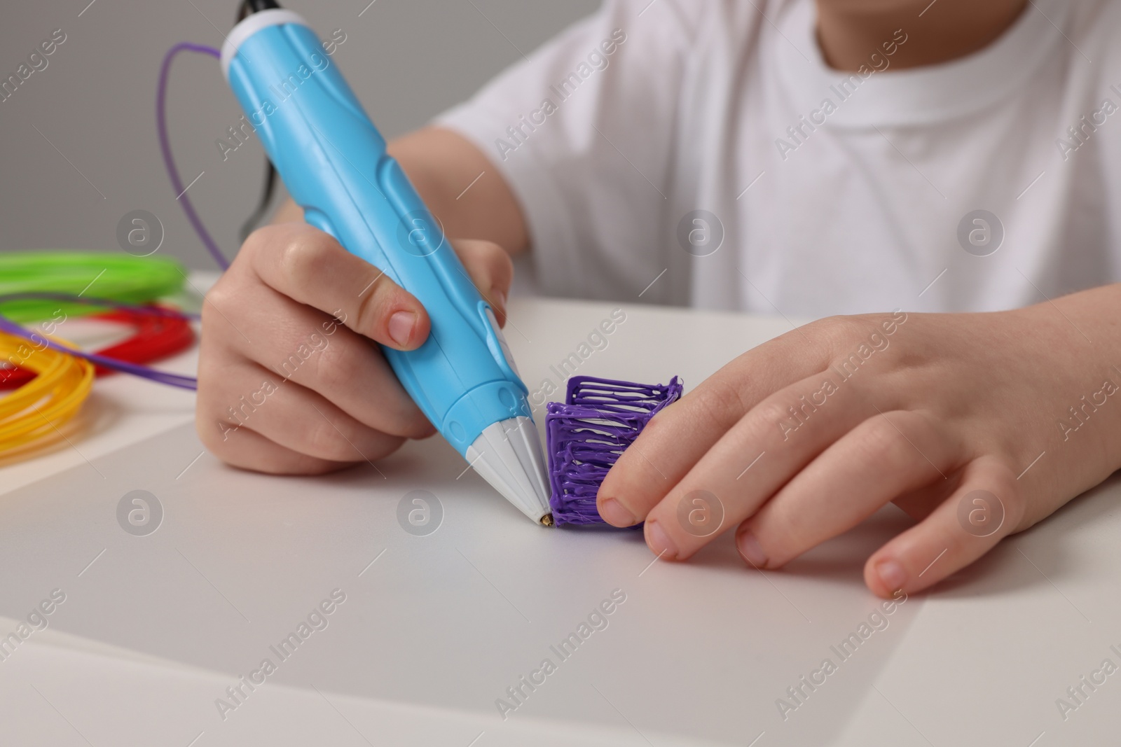 Photo of Boy drawing with stylish 3D pen at white table, closeup