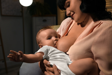 Photo of Woman breastfeeding her little baby on sofa in evening