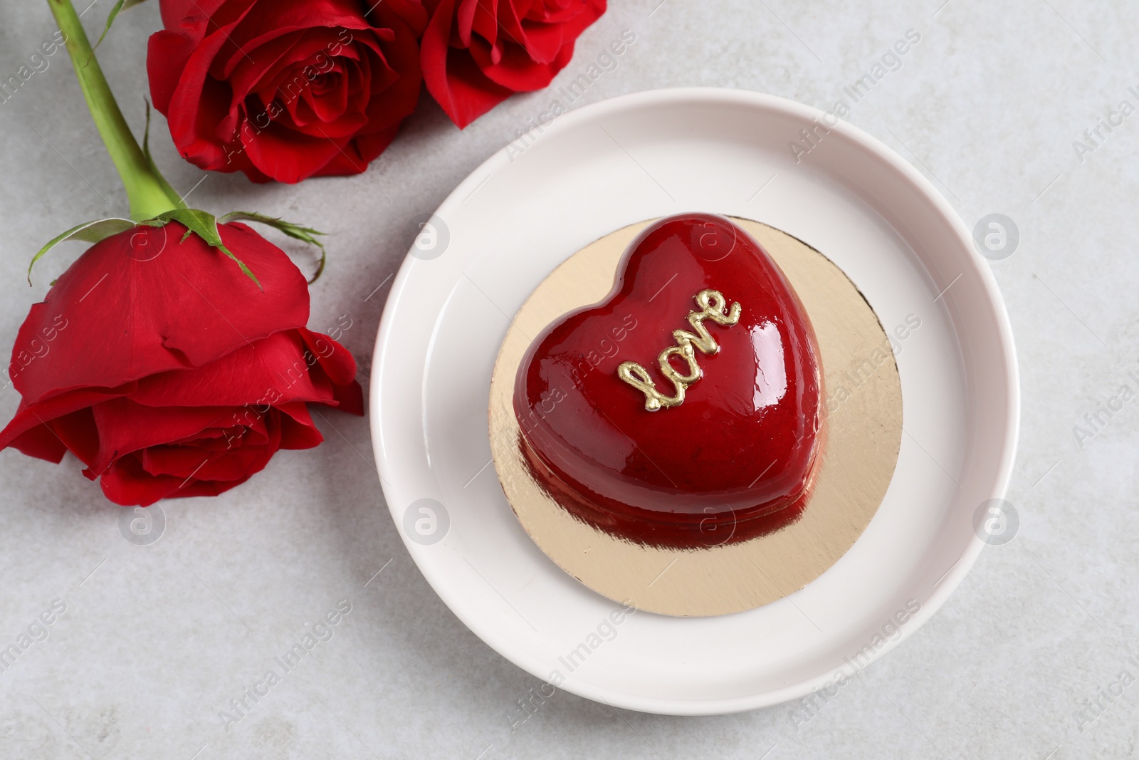 Photo of St. Valentine's Day. Delicious heart shaped cake and roses on light table, flat lay