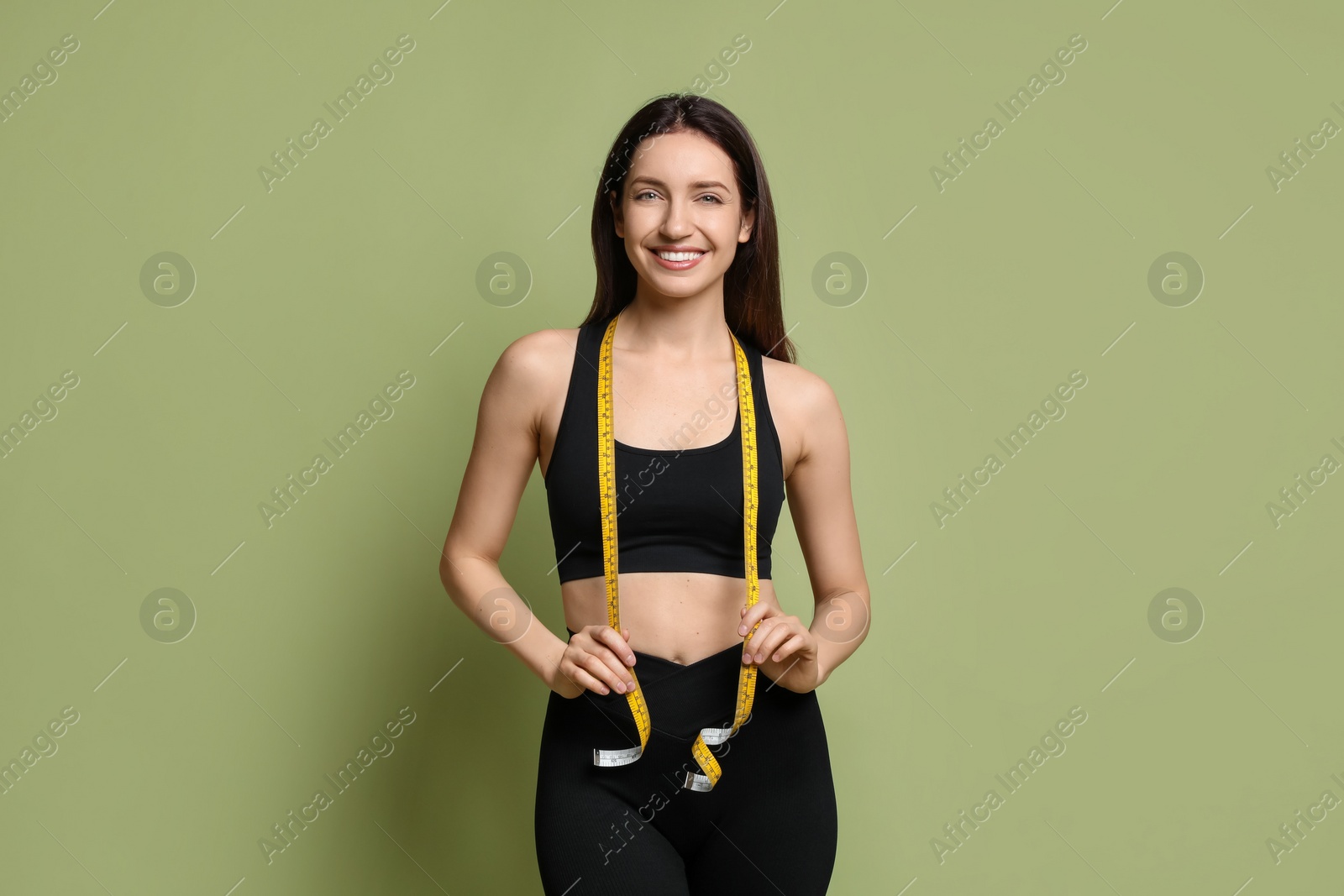 Photo of Happy young woman with measuring tape showing her slim body on green background