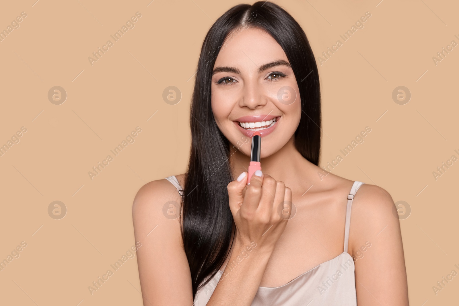 Photo of Young woman applying nude lipstick on beige background