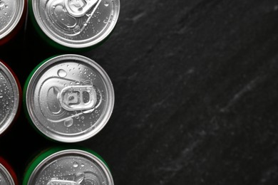 Photo of Energy drink in wet cans on black textured background, top view. Space for text